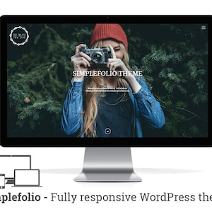 Pode incluir: Uma mulher usando um chapéu vermelho e uma jaqueta de jeans azul está segurando uma câmera vintage na frente do rosto. A imagem é exibida em uma tela de computador com o texto "Simplefolio Theme" na tela.