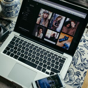 Puede incluir: Un ordenador port&aacute;til plateado con un teclado negro y un trackpad blanco. El port&aacute;til est&aacute; abierto y muestra un sitio web con un fondo negro y texto blanco. El sitio web presenta fotos de personas y texto que dice "Nessa".