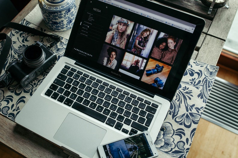 Puede incluir: Un ordenador port&aacute;til plateado con un teclado negro y un trackpad blanco. El port&aacute;til est&aacute; abierto y muestra un sitio web con un fondo negro y texto blanco. El sitio web presenta fotos de personas y texto que dice "Nessa".