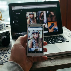 Puede incluir: Un tel&eacute;fono inteligente blanco con una mujer de cabello rubio y ojos azules que lleva una bufanda estampada en la pantalla. El tel&eacute;fono est&aacute; en la mano de una persona.