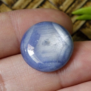 Puede incluir: Una piedra preciosa redonda y azul con un patrón en forma de estrella en el centro. La piedra preciosa es lisa y pulida.