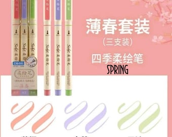 May include: A set of three pastel colored fine-tip markers with a light brown barrel. The markers are labeled "Soft 柔绘笔" and are packaged in a light brown box with the text "薄春套装 (三支装) 四季柔绘笔 SPRING" in black. The markers are shown with their corresponding colors: light pink, light purple, and light green. The text "薄樱", "白堇", and "子衿" are shown below the color swatches.