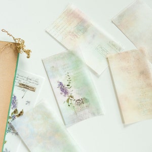 May include: Five sheets of translucent paper with a watercolor background and floral designs. The paper has a vintage aesthetic with faded text and stamps.