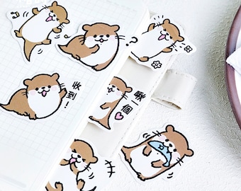 May include: A collection of cute otter stickers in various poses, with brown and white fur, and expressive faces. Some stickers have speech bubbles with text. The stickers are placed on a white notebook page.