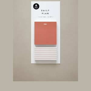 May include: A pack of 100 sticky notes with a daily planner theme. The notes are 52 x 54 mm and are made of paper. The top note is a solid orange color with the text "say," printed in white. The bottom note is white with lined paper.