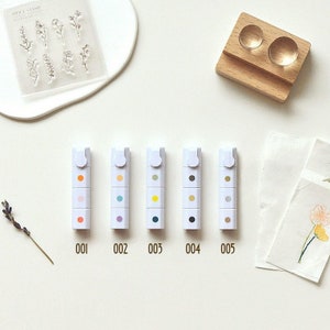 May include: Five sets of colourful ink pads for stamping. Each set contains five different colours of ink pads in a white plastic case. The ink pads are labelled 001, 002, 003, 004, and 005.