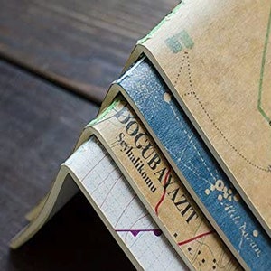 May include: Stack of four vintage notebooks with a map design on the cover. The top notebook has the text "Dogubayazit" and "Seyahatlikomu" printed on the spine.