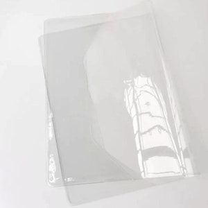 Puede incluir: Un protector de hojas de pl&aacute;stico transparente, dise&ntilde;ado para proteger documentos u otros materiales de da&ntilde;os. El protector est&aacute; doblado por la mitad, mostrando su superficie lisa y transparente.
