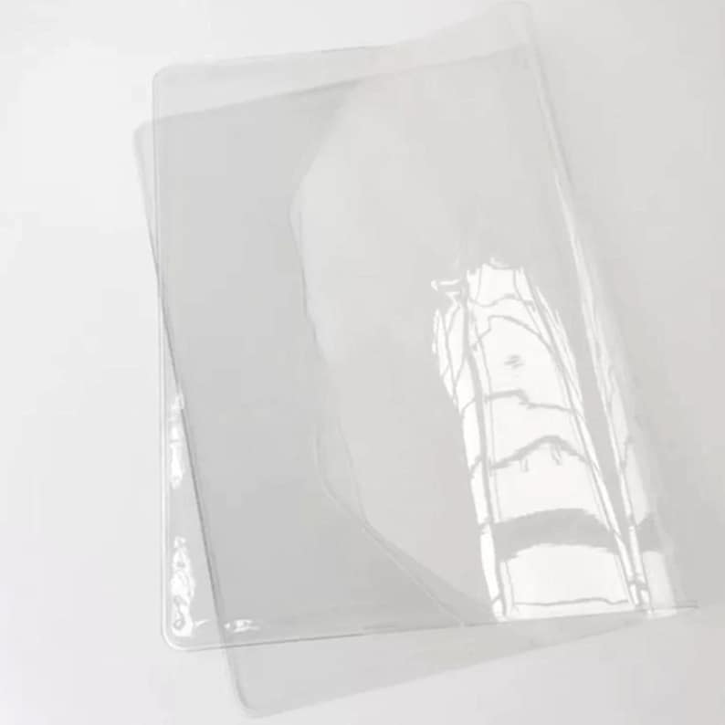 Puede incluir: Un protector de hojas de pl&aacute;stico transparente, dise&ntilde;ado para proteger documentos u otros materiales de da&ntilde;os. El protector est&aacute; doblado por la mitad, mostrando su superficie lisa y transparente.
