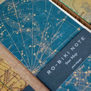 May include: A blue notebook with a star map printed on the cover. The notebook has a black spine with the text "RO-BIKI NOTE" and "Star Map" printed in white. The text "plain 60 pages" is also printed in white.