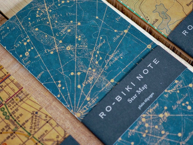 May include: A blue notebook with a star map printed on the cover. The notebook has a black spine with the text "RO-BIKI NOTE" and "Star Map" printed in white. The text "plain 60 pages" is also printed in white.