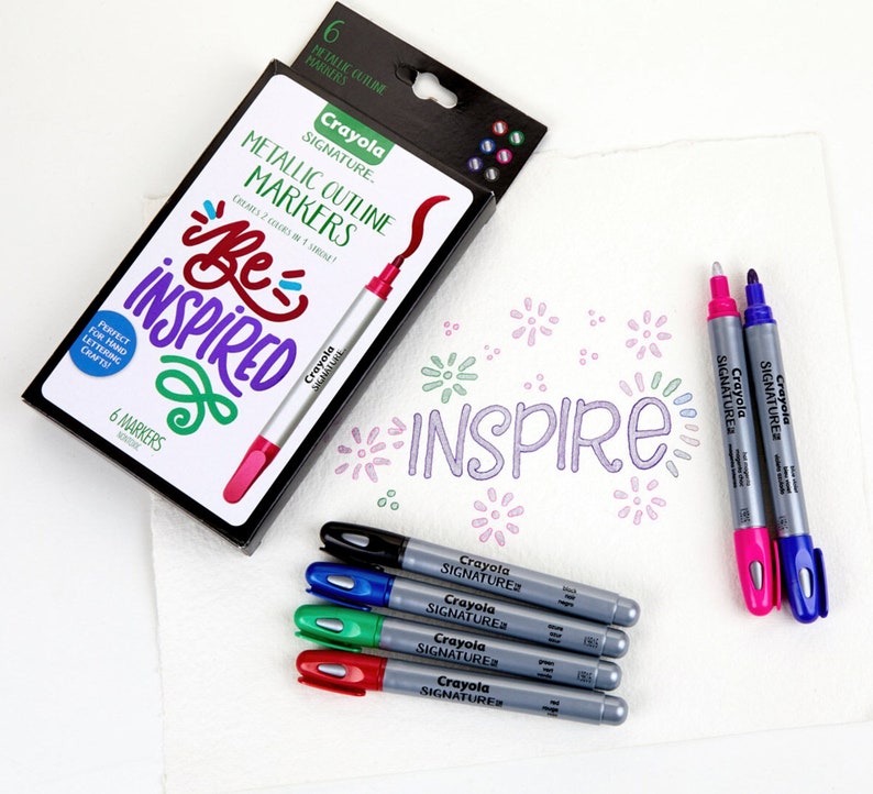 May include: A set of six metallic outline markers in a black box with the words "Crayola Signature Metallic Outline Markers" and "Be Inspired". The markers are in colors like pink, green, blue, and black. The box also includes a sample of the markers used to write the word "Inspire" on a white surface.