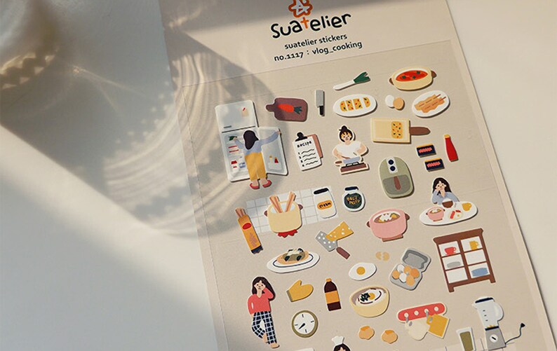 Pu&ograve; includere: Un foglio di adesivi colorati con illustrazioni di cibo, elettrodomestici da cucina e persone che cucinano. Gli adesivi sono etichettati "Suatelier stickers no.1137 : vlog_cooking".