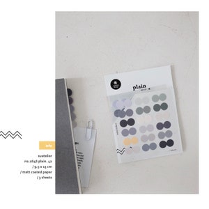 May include: A pack of gray, white, and black dot stickers with the text "plain DECO X" on the front. The stickers are on a clear plastic sheet. The pack is labeled "suatelier no.1646 plain. 42 / 9.5 x 13 cm / matt coated paper / 3 sheets".