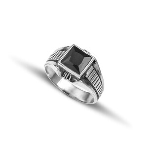 May include: A silver ring with a black square-shaped gemstone set in a textured band.