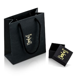 May include: Black gift bag with black handles and gold lettering that says "Xeil&aacute;s Aidonou 47". A smaller black box with gold lettering that says "Xeil&aacute;s Aidonou 47" is sitting in front of the bag.