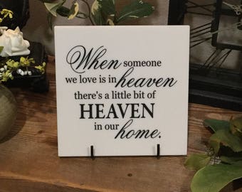 May include: White ceramic sign with black text that reads "When someone we love is in heaven there's a little bit of HEAVEN in our home."