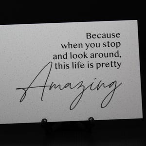 May include: White sign with black text that reads "Because when you stop and look around, this life is pretty amazing".