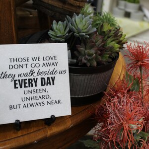 May include: A white sign with black text that reads "Those we love don't go away they walk beside us every day unseen, unheard, but always near."