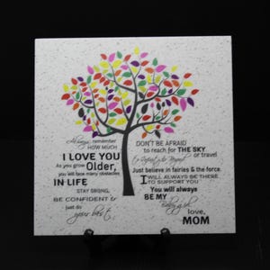 May include: A white square tile with a colorful tree design and a message that reads "I love you. As you grow older, you will face many obstacles in life. Stay strong, be confident & just do your best. Don't be afraid to reach for the sky or travel. Just believe in fairies & the force. I will always be there to support you. You will always be my... love, Mom."