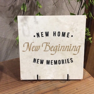 May include: A white marble sign with black text that reads "New Home. New Beginning. New Memories".