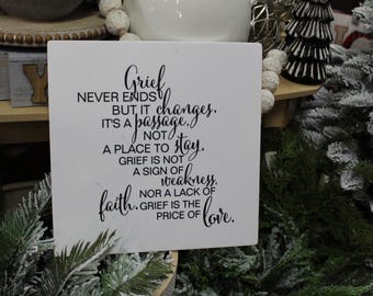 May include: White wooden sign with black text that reads "Grief never ends but it changes. It's a passage, not a place to stay. Grief is not a sign of weakness, nor a lack of faith. Grief is the price of love."