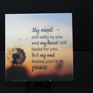 May include: A white ceramic tile with a quote about peace and a dandelion in the background. The quote reads: "My mind still talks to you and my heart still looks for you. But my soul knows you're at peace."