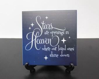 May include: A blue and white ceramic tile with a quote about stars being openings in heaven where loved ones shine down. The tile is on a black stand.