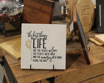 May include: A white sign with black text that reads "the best things in LIFE are the people we love, the places we've been and the memories we've made along the way."