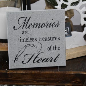 May include: A gray stone plaque with the text "Memories are timeless treasures of the Heart" in black lettering. The plaque is sitting on a wooden surface.