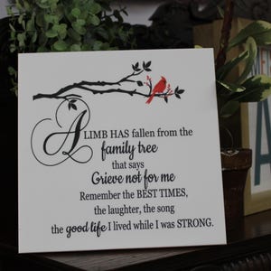 May include: A white wooden sign with a black silhouette of a tree branch with a red cardinal perched on it. The sign has a black inscription that reads "A limb has fallen from the family tree that says Grieve not for me. Remember the best times, the laughter, the song the good life I lived while I was strong."