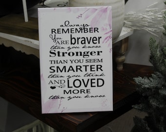 May include: White wooden sign with pink floral design and black text that reads "always REMEMBER You ARE braver than you know. Stronger THAN YOU SEEM SMARTER than you think AND LOVED MORE than you know."