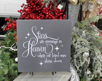 May include: A gray wooden sign with white lettering that reads "Stars are openings in Heaven where our loved ones shine down". The sign is surrounded by greenery and red berries.