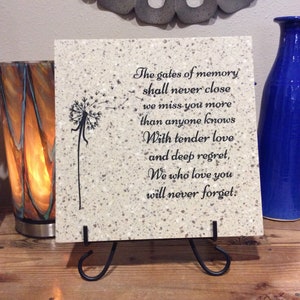 May include: A white ceramic tile with a black dandelion design and a quote about memory. The quote reads: "The gates of memory shall never close we miss you more than anyone knows With tender love and deep regret, We who love you will never forget."