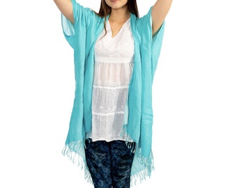 May include: A woman wearing a light blue, open-front, long-sleeved, fringed cardigan over a white, lace-trimmed blouse and dark blue patterned leggings.