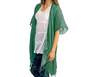 May include: A green linen kimono with a fringed hem. The kimono has short sleeves and is open at the front. The model is wearing a white top and blue jeans.