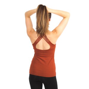 May include: A rust-coloured tank top with a criss-cross back design. The tank top is made of a soft, stretchy fabric and has a relaxed fit.