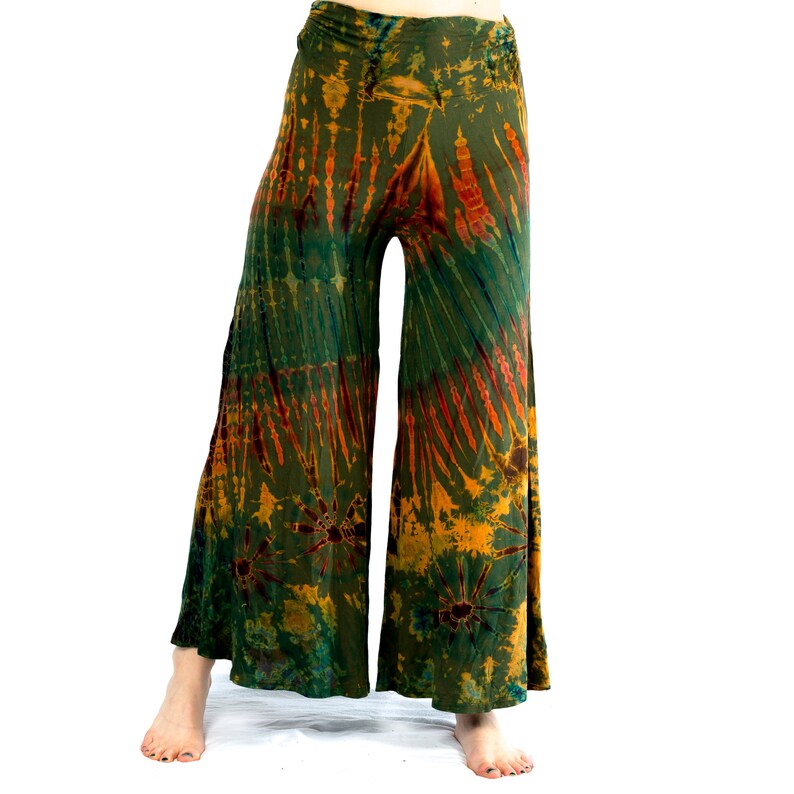 May include: Tie-dye wide-leg trousers in green, orange, and yellow. The trousers have an elasticated waistband and a flowing shape. The tie-dye design features vertical and circular patterns. The trousers are made of a soft, flowing fabric.