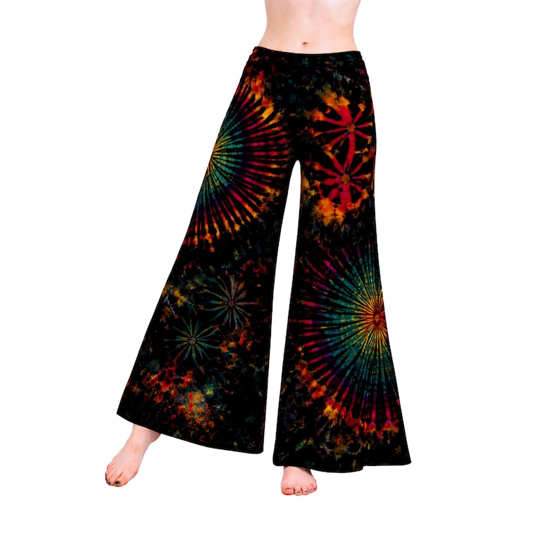May include: Black flared trousers with a vibrant tie-dye pattern in shades of red, orange, yellow, green, and blue. The design features circular and starburst patterns. The trousers have a high waist and a wide leg opening.
