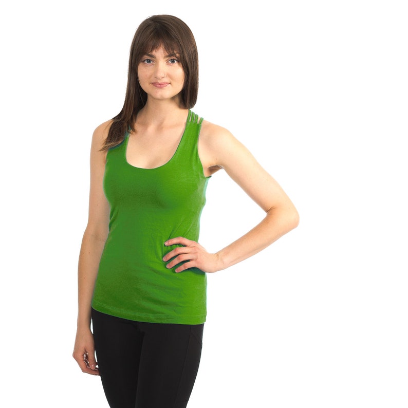 May include: A woman wearing a bright green tank top and black trousers. She is standing with her hand on her hip and looking at the camera.