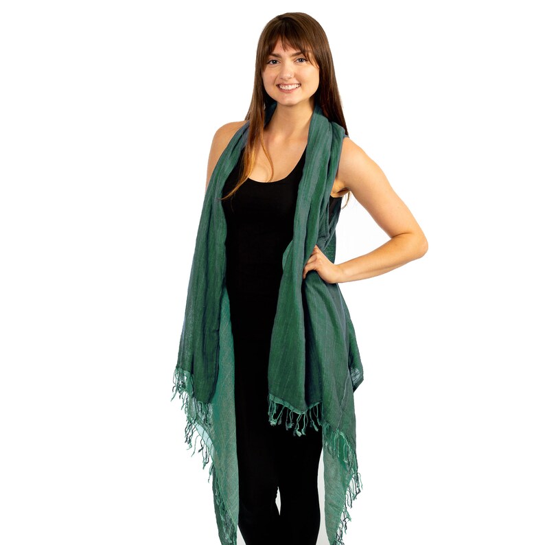 May include: A teal blue cotton scarf with fringe edges. The scarf is draped over a person's shoulders and tied at the neck.