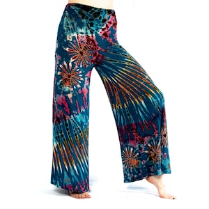 May include: Teal tie-dye wide-leg trousers featuring a pattern of orange, pink, and yellow. The fabric has a soft, flowing appearance, with a high waist and a relaxed fit. The tie-dye design radiates from the center.