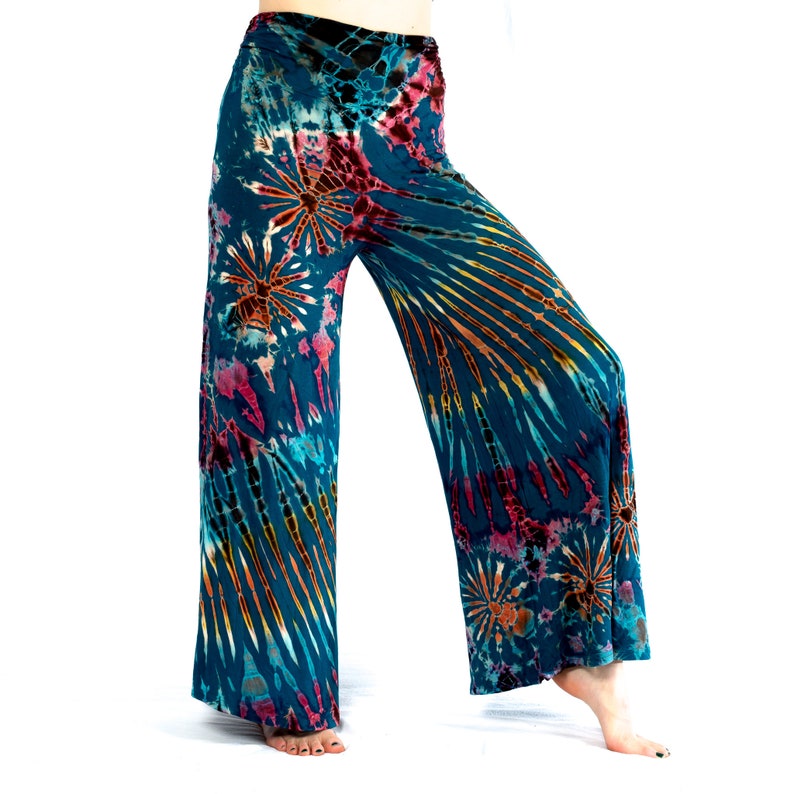 May include: Teal tie-dye wide-leg trousers featuring a pattern of orange, pink, and yellow. The fabric has a soft, flowing appearance, with a high waist and a relaxed fit. The tie-dye design radiates from the center.