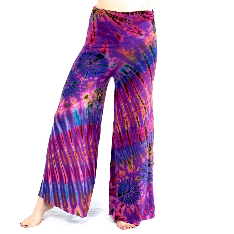 May include: Wide-leg trousers with a vibrant tie-dye pattern in shades of purple, pink, blue, and orange. The fabric appears soft and flowing, with a high, wide waistband. The tie-dye design features radial and striped patterns.