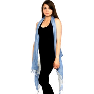 May include: A woman wearing a black vest top and a light blue scarf draped around her neck. The scarf has a fringed edge and is tied at the back.