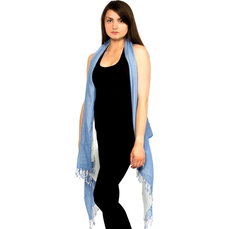 May include: A woman wearing a black vest top and a light blue scarf draped around her neck. The scarf has a fringed edge and is tied at the back.