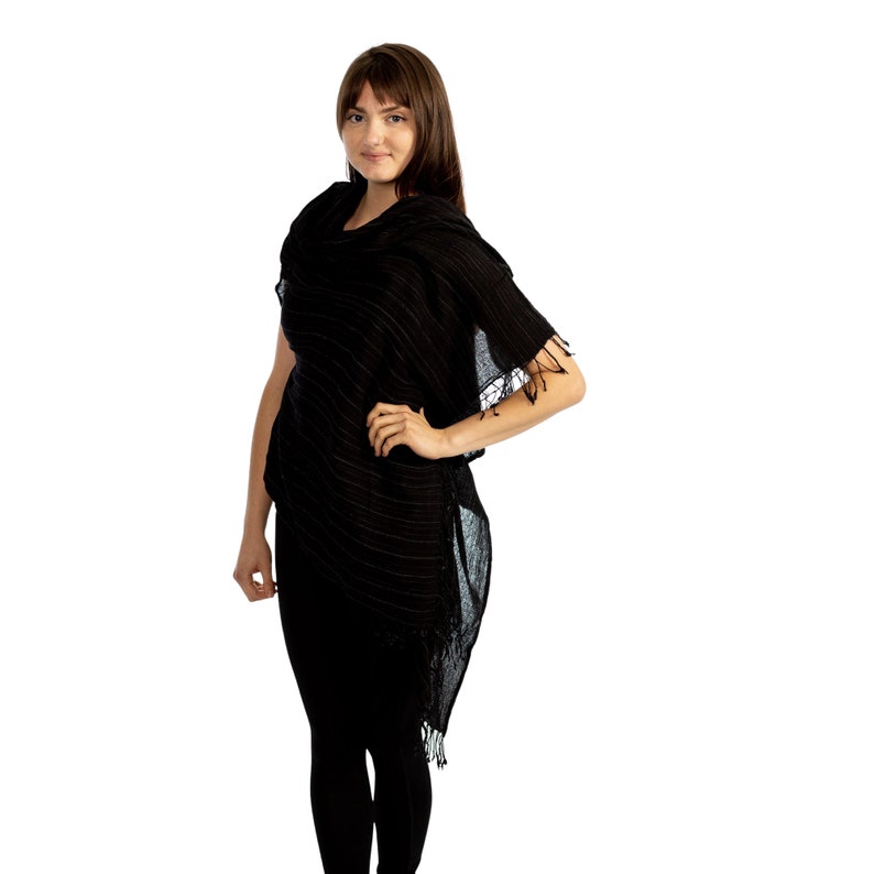 May include: A black and white striped poncho with a fringe trim. The poncho is made of a lightweight fabric and has a relaxed fit.