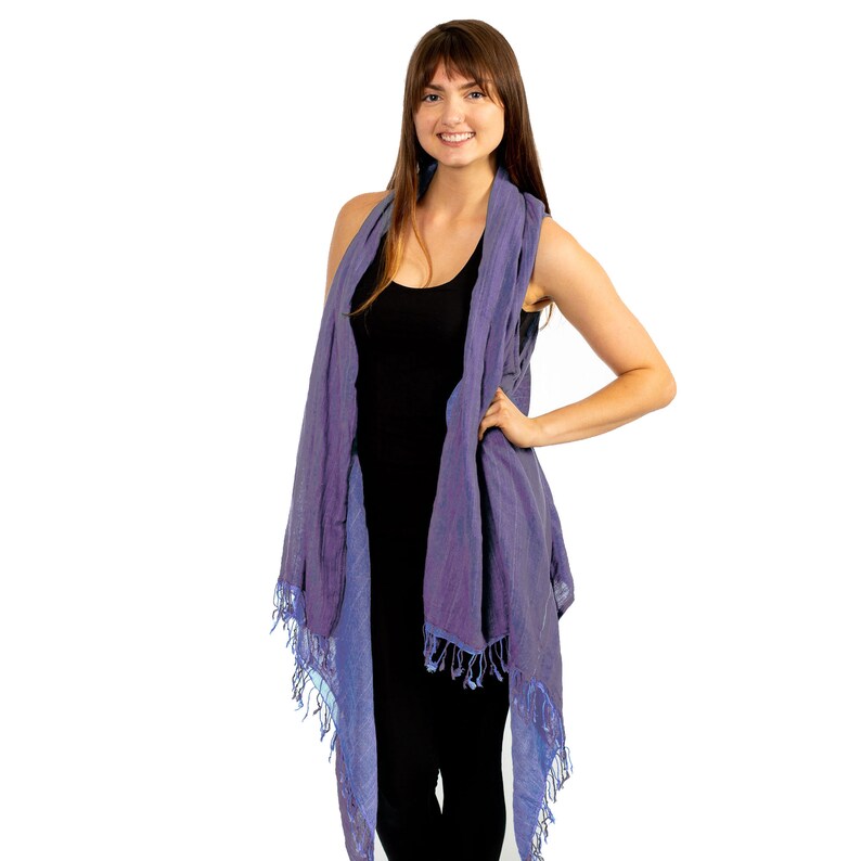 May include: A woman wearing a purple and blue fringed shawl over a black vest top and black trousers.
