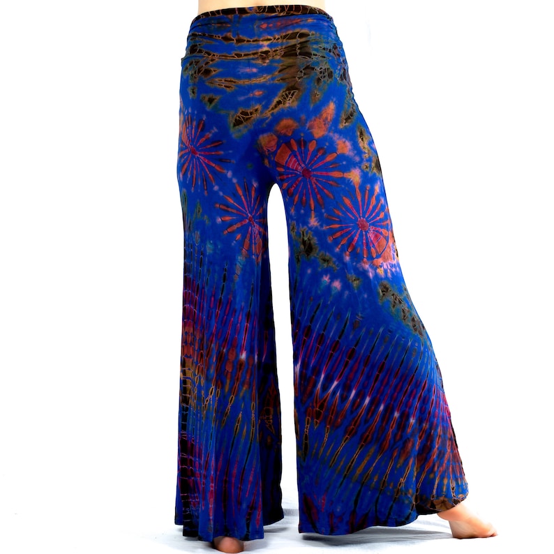 May include: Tie-dye wide-leg trousers in blue, brown, and red. The fabric has a flowing drape, with a high, elasticated waistband. The design features starburst and striped patterns. Measurements are in centimetres.