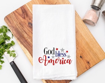 May include: White kitchen towel with the text "God Bless America" in black lettering with red and blue stars.